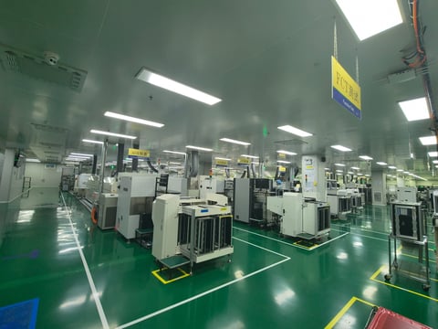 Manufacturing facility with rows of industrial machines on green flooring under bright fluorescent lighting
